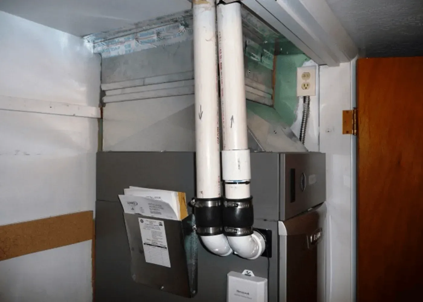 Gray high-efficiency furnace with white PVC exhaust and intake pipes attached via black rubber couplers.