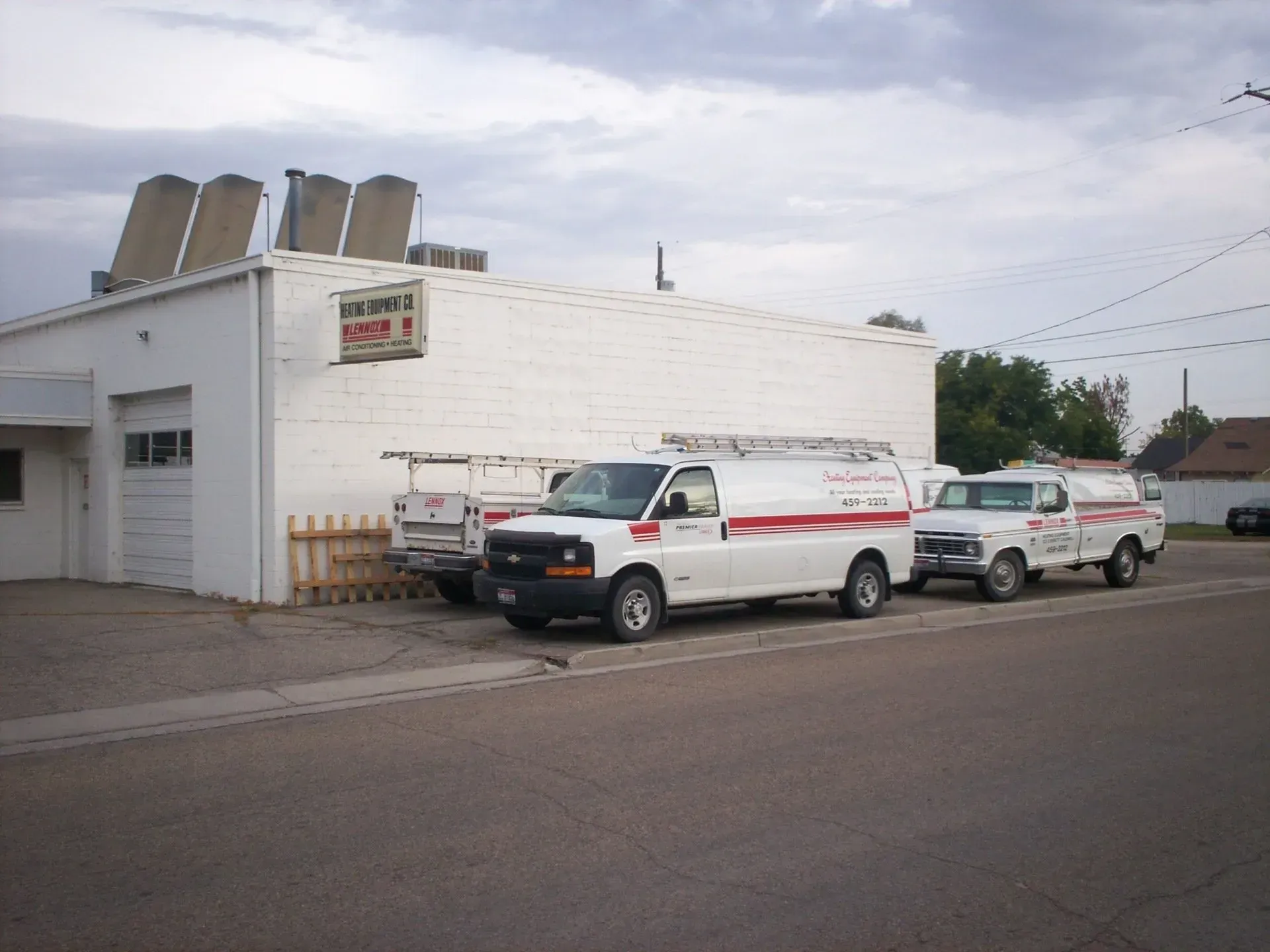 A white commercial building with work vans parked in front, featuring a sign for a plumbing and heating company.