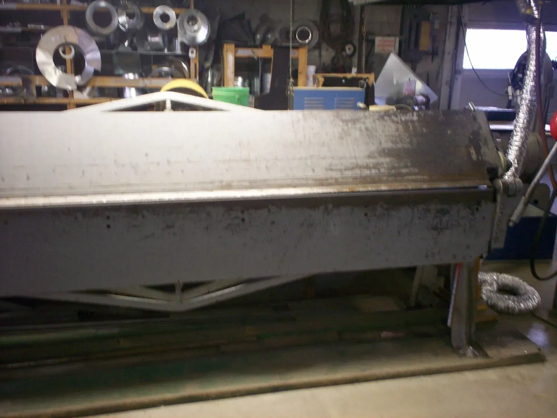 A large, industrial metal bending machine or brake centered in a cluttered workshop.