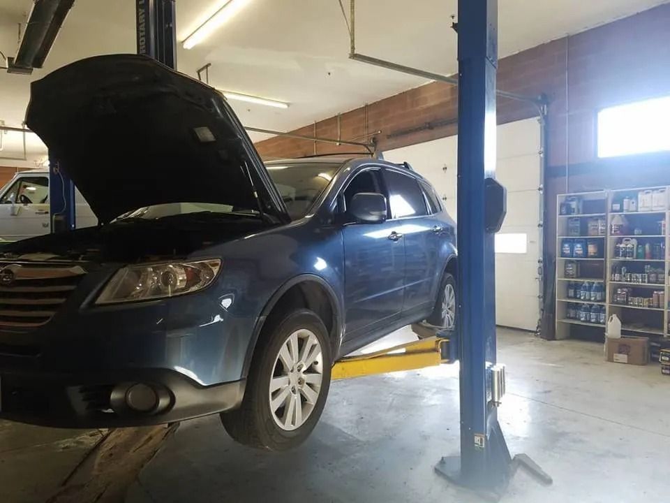 Blue SUV on a car lift in a garage with the hood open.