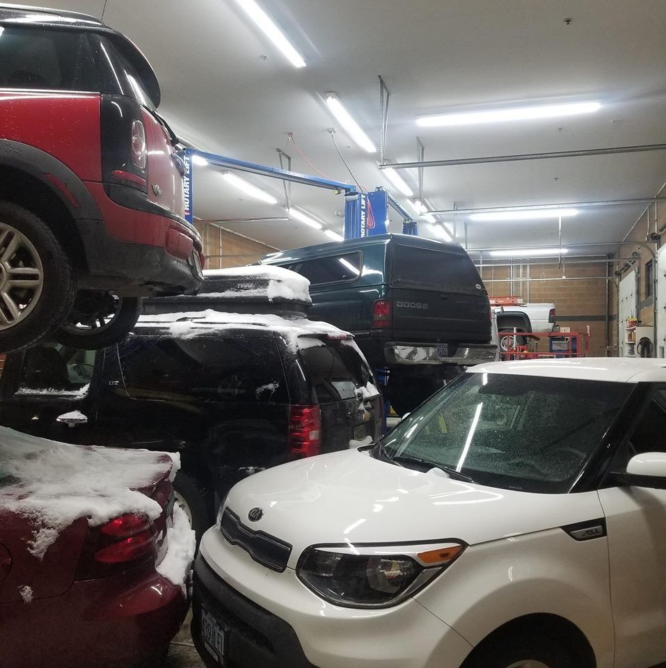 Cars in a mechanic shop: red Mini Cooper on a lift, plus SUVs and a white Kia Soul.