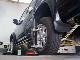 Black truck undergoing wheel alignment; tire has alignment equipment attached.