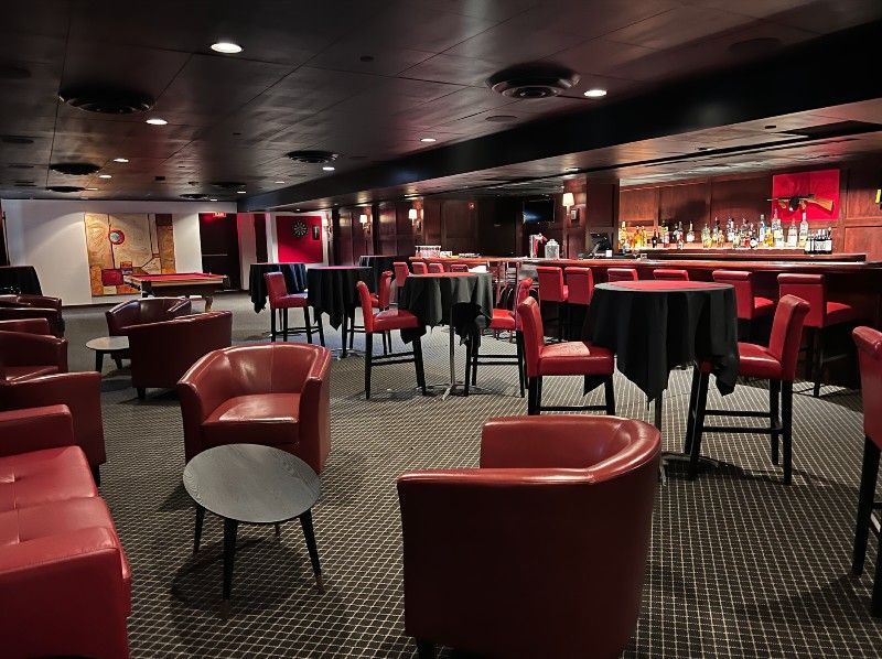 Red-themed bar with tables, chairs, and a bar. Black tablecloths, red seating, and a dark interior.