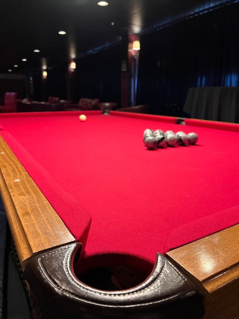 Red felt pool table with balls set up, low-lit bar setting.