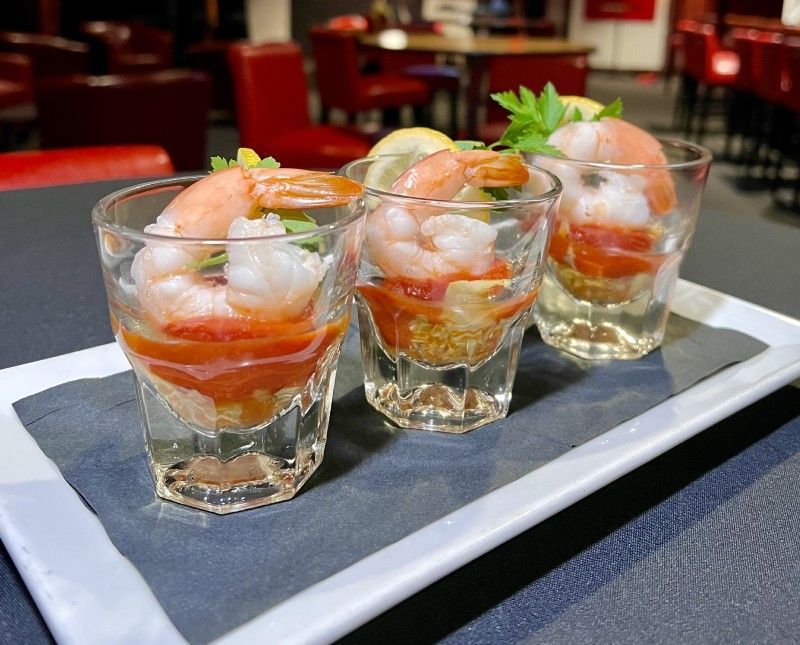 Shrimp cocktail appetizers in shot glasses, layered over sauce, garnished with lemon and parsley.