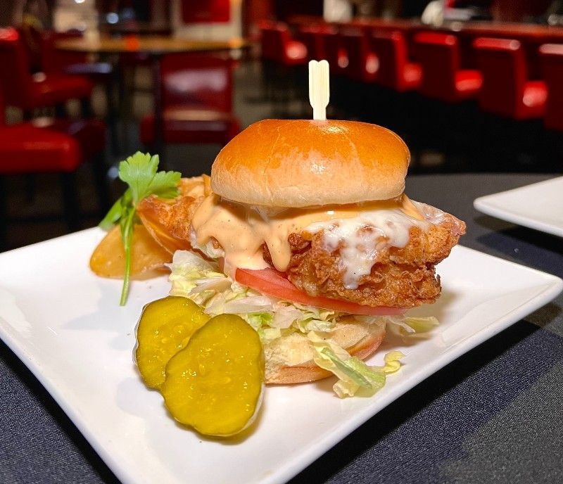 Fried chicken sandwich with pickles and a potato wedge on a white plate.
