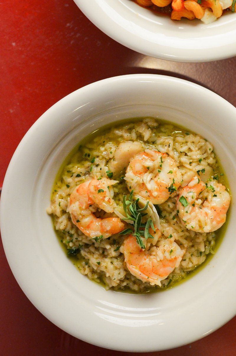 Bowl of shrimp risotto on a red surface. Five shrimp are visible.