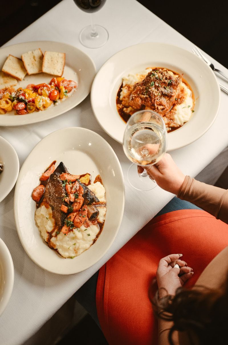 Gourmet meal: three plates on a white tablecloth. A person holding a wine glass, red chair.