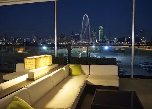 Rooftop lounge with white sofas and a city skyline at night.