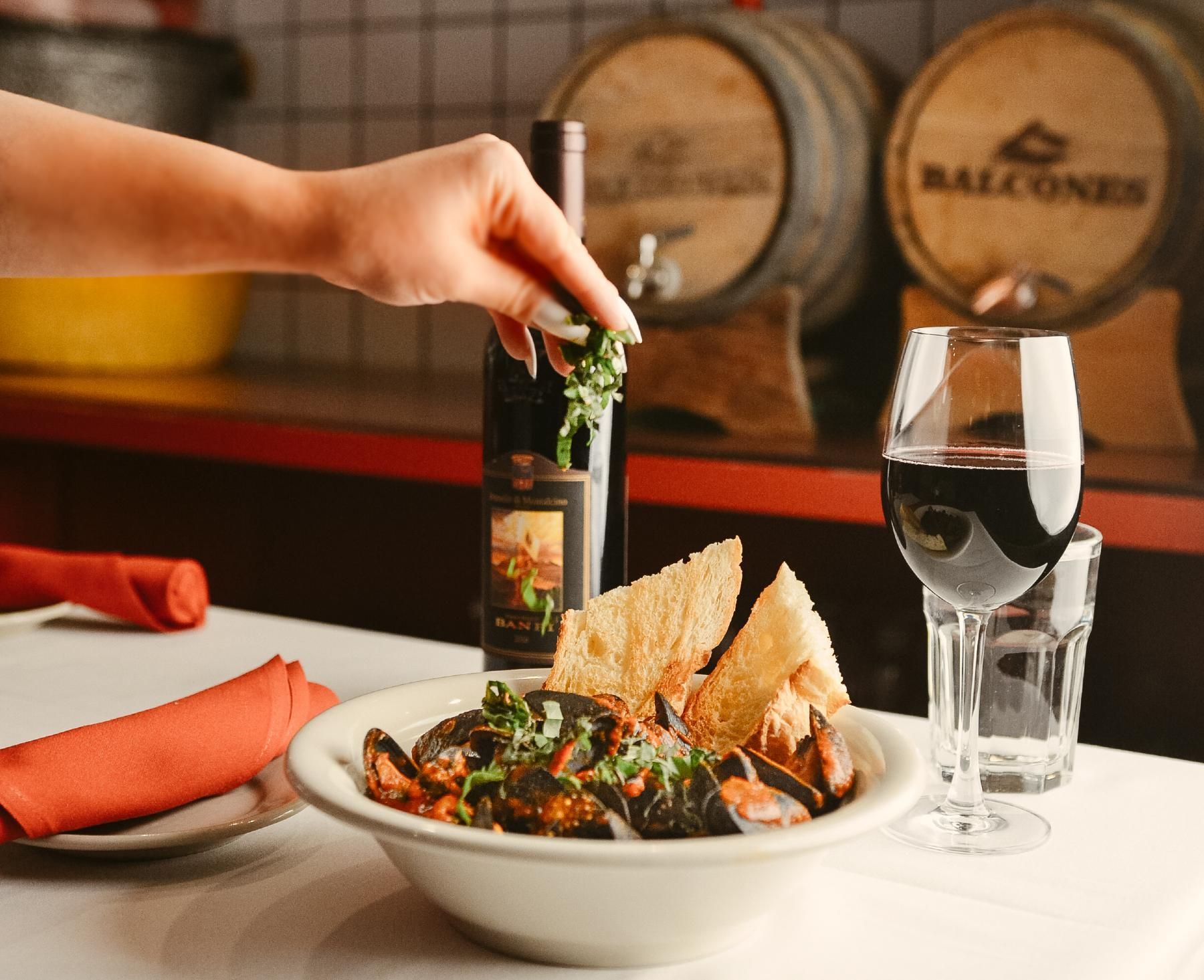 Person adding herbs to mussels with toast and red wine, set on a table in a restaurant.
