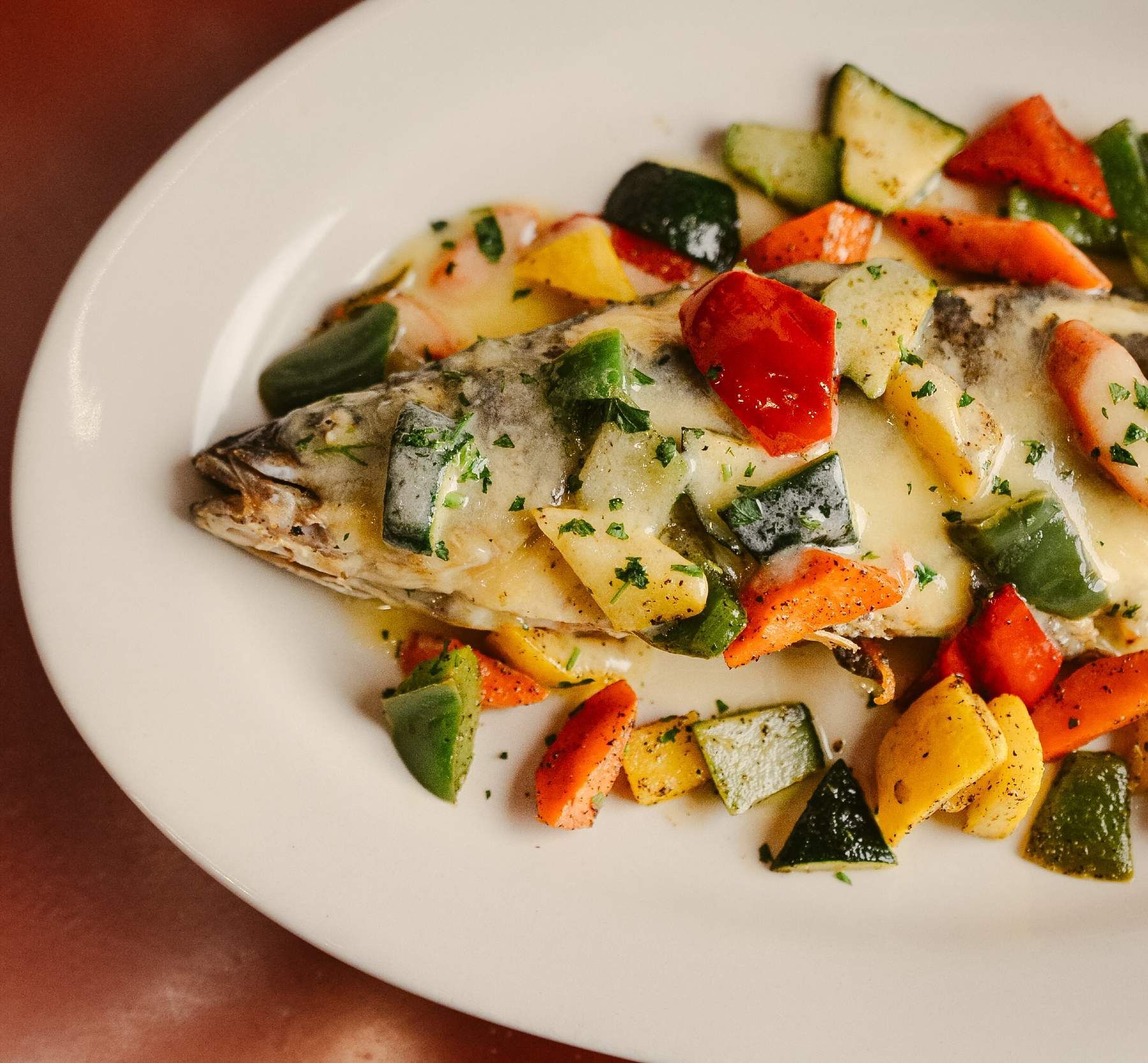 Baked fish with colorful vegetables on a white plate.