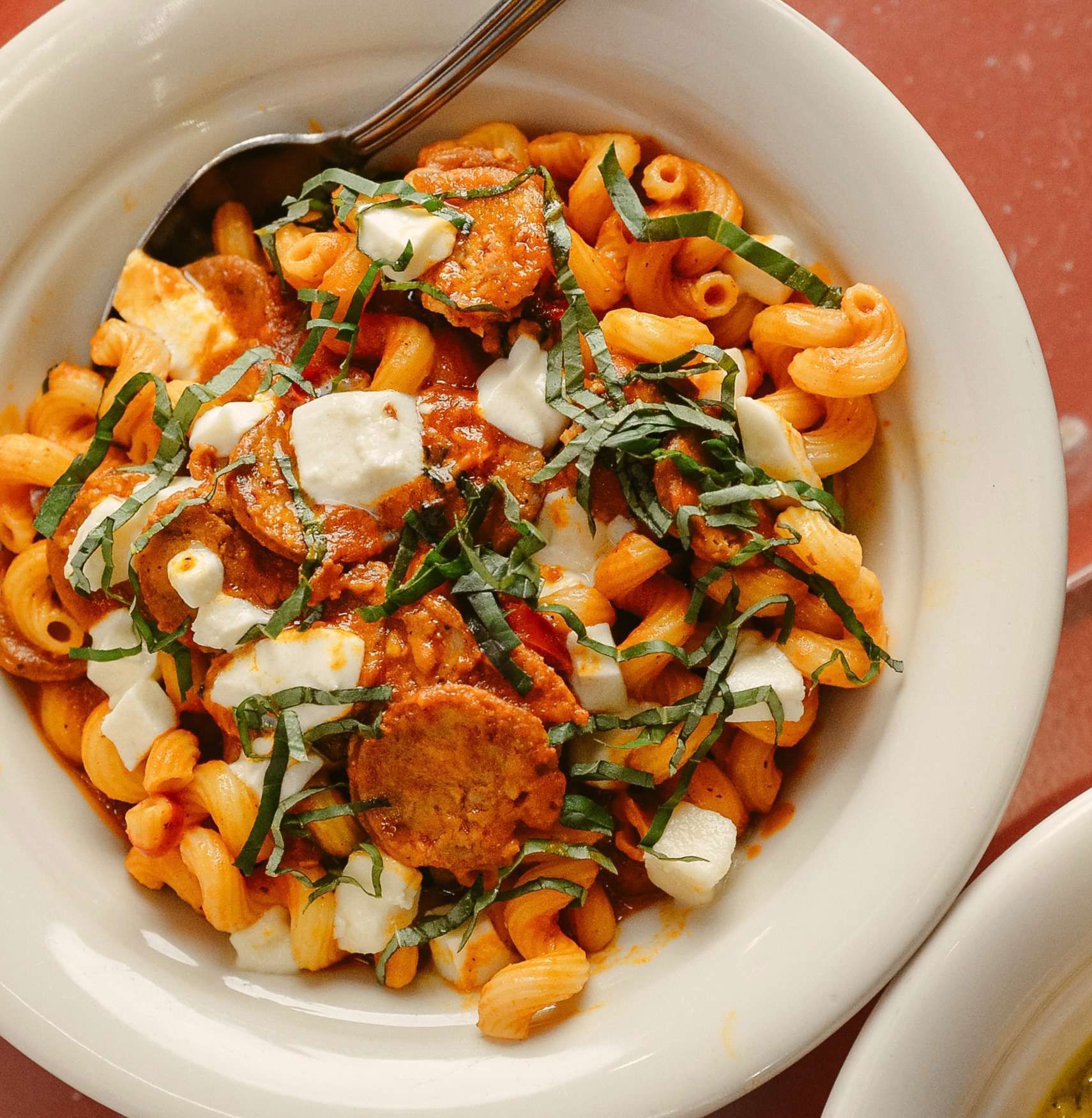 Bowl of macaroni pasta with sauce, sausage, mozzarella, and basil.