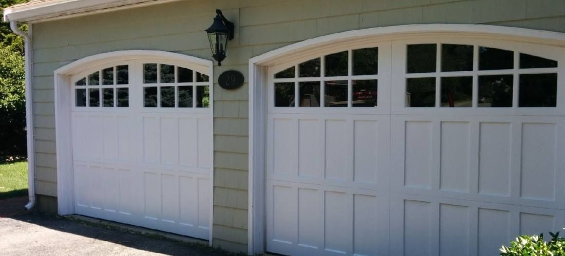 A pair of white garage doors with arched windows on a house.