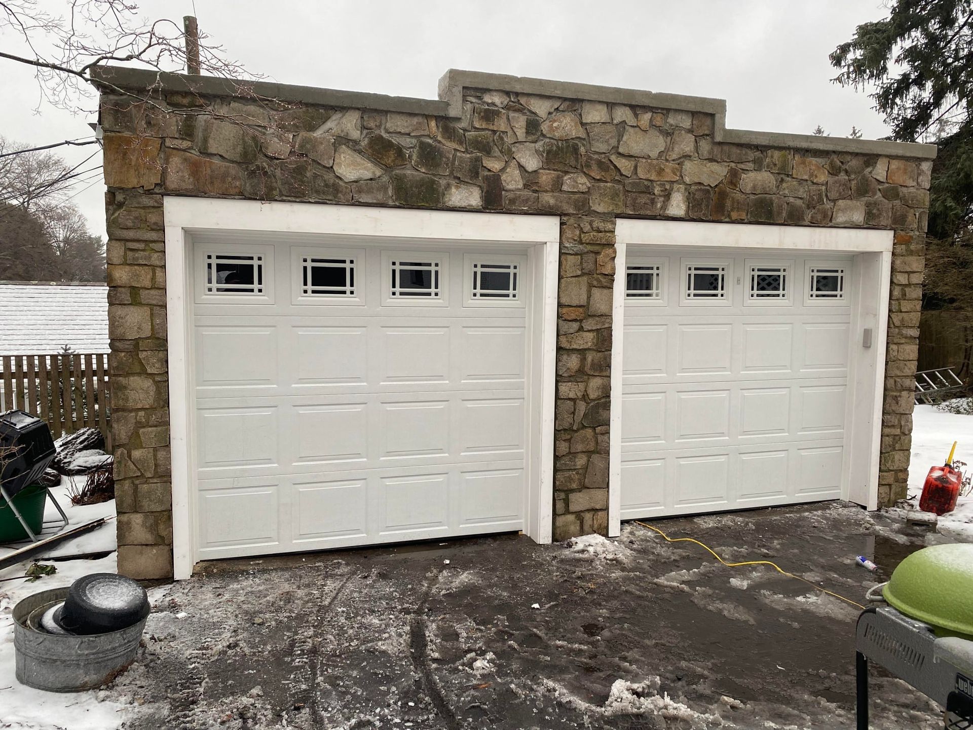 A garage with two white garage doors and a stone wall.