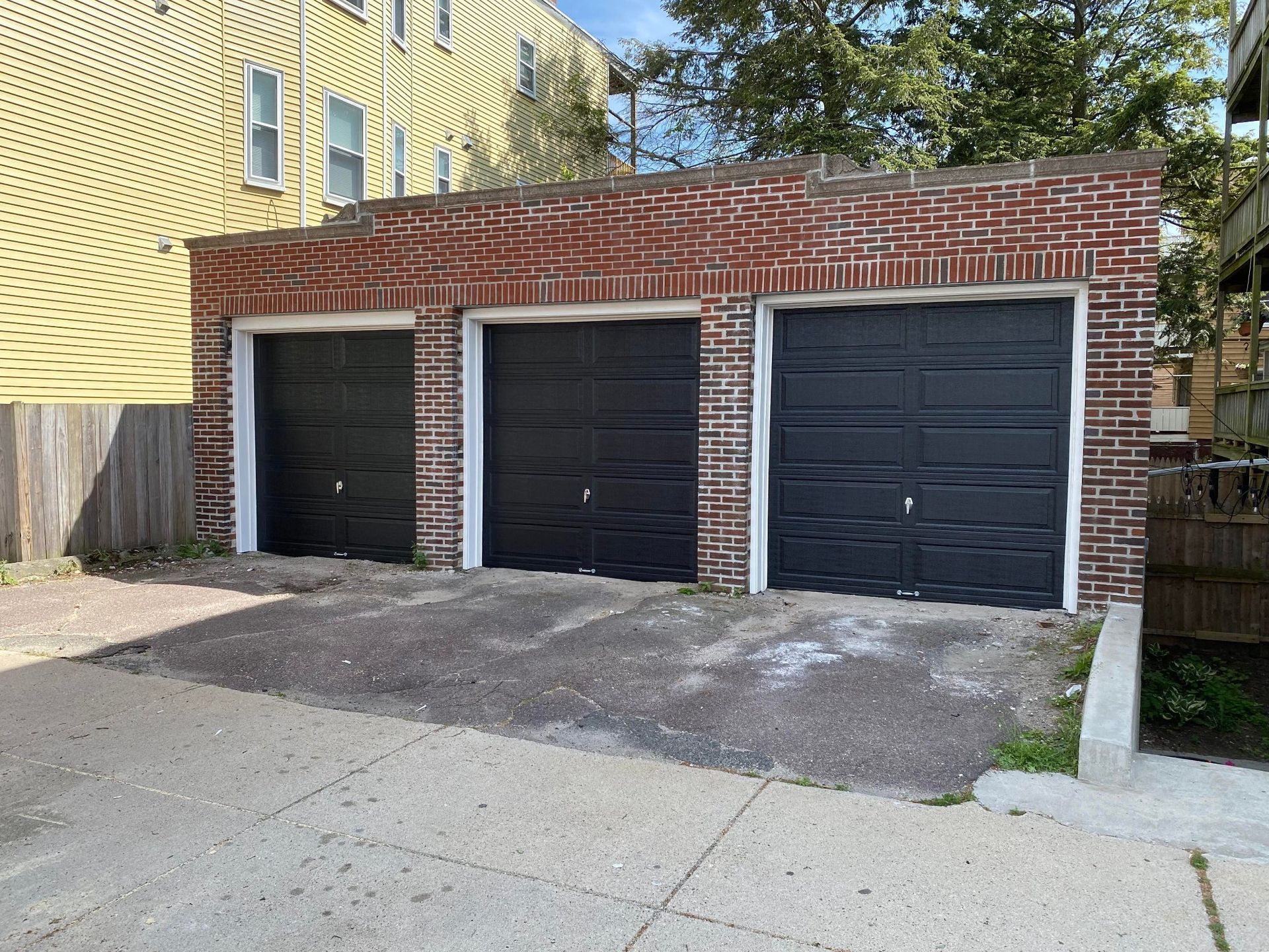 Three black garage doors are sitting next to each other in front of a brick building.