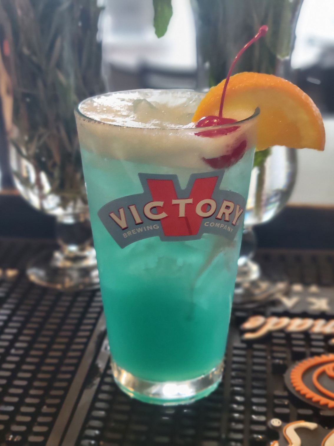A blue drink in a victory glass with a cherry on top