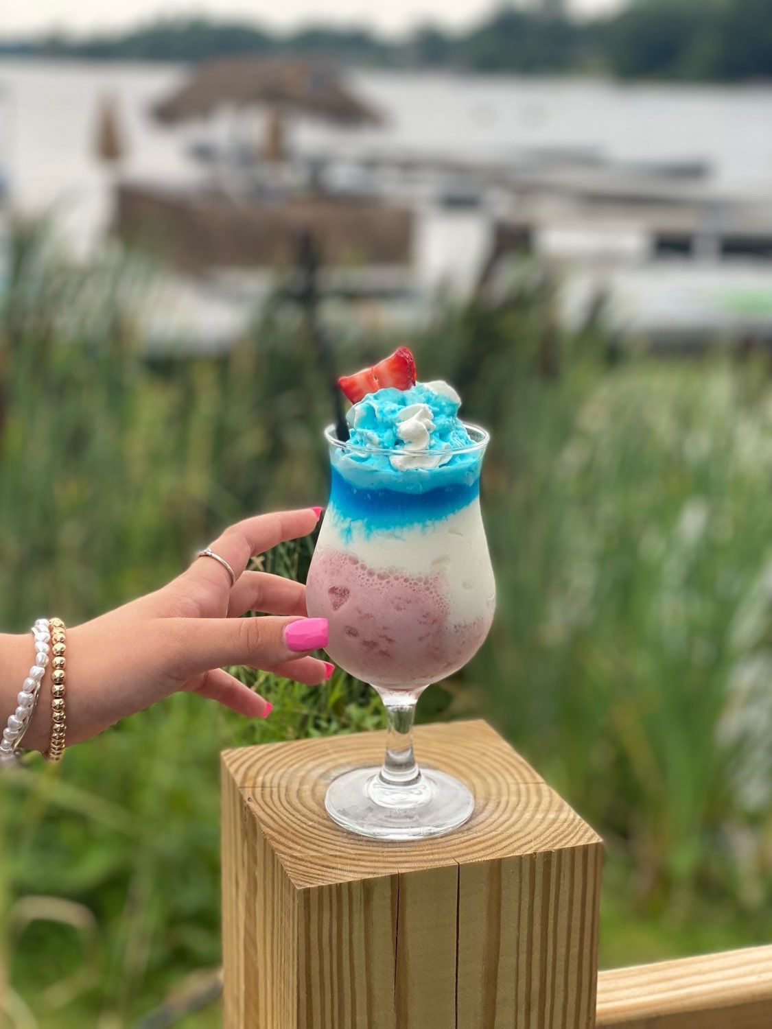 A woman is holding a glass of ice cream on a wooden post.