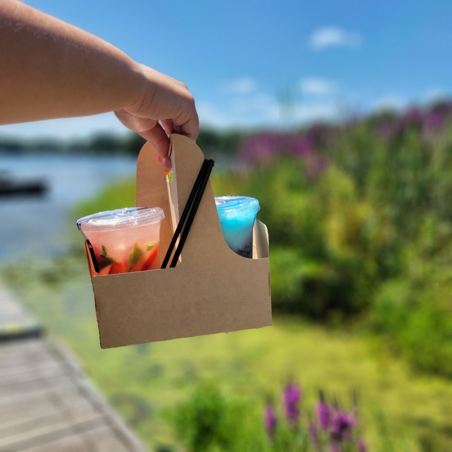 A person is holding a cardboard carrier with two cups in it