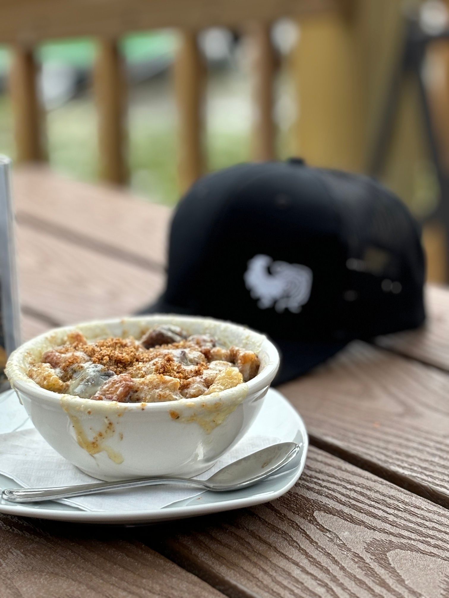A bowl of soup is sitting on a plate on a wooden table next to a hat.