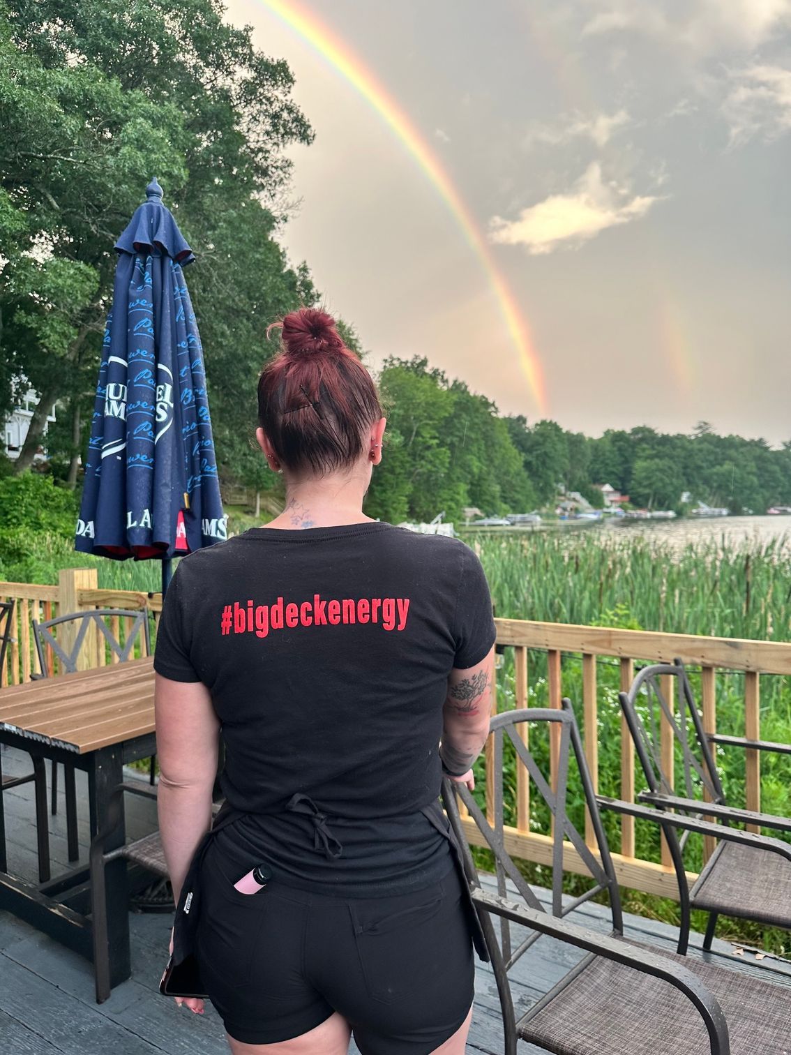 A woman is standing on a deck with a rainbow in the background.