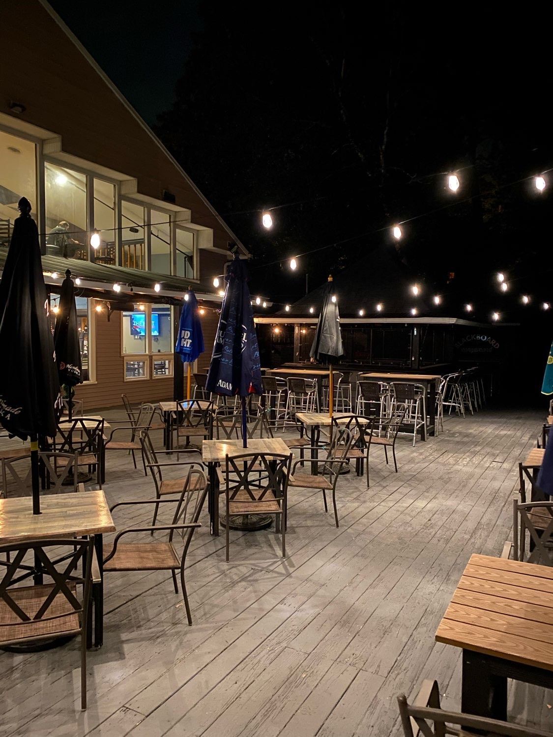 There are many tables and chairs on the deck at night.