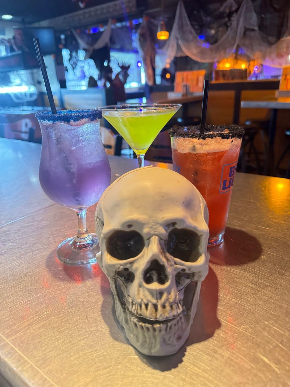 A skull is on a table next to three drinks.