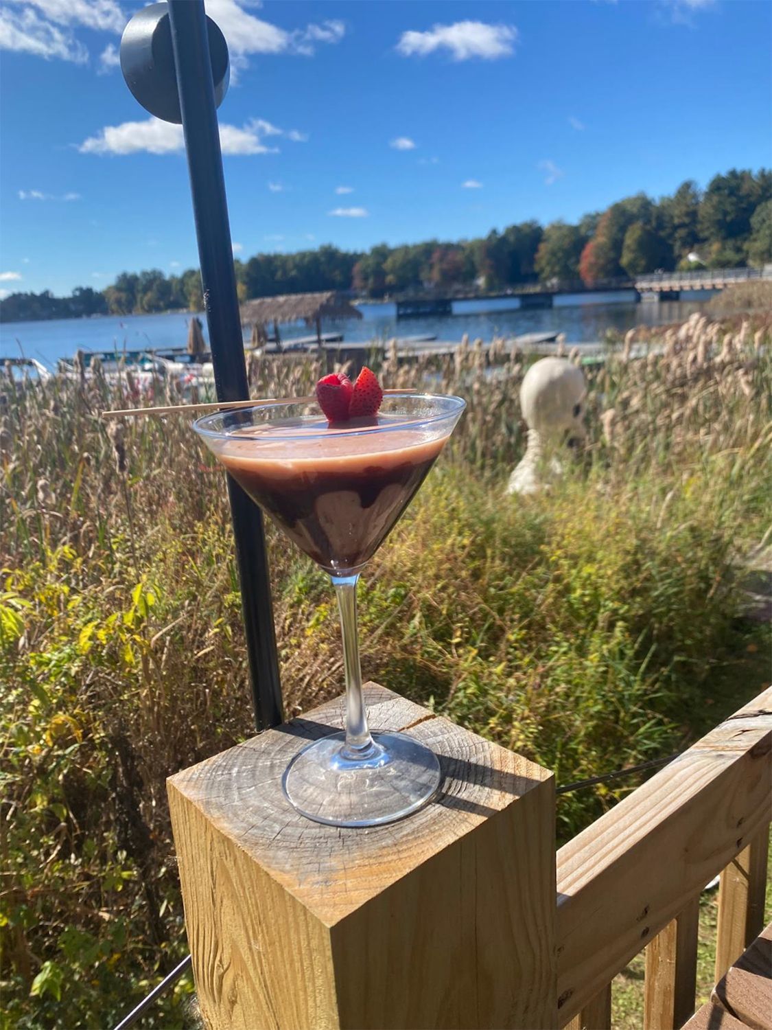 A martini with a strawberry on top is sitting on a wooden railing.