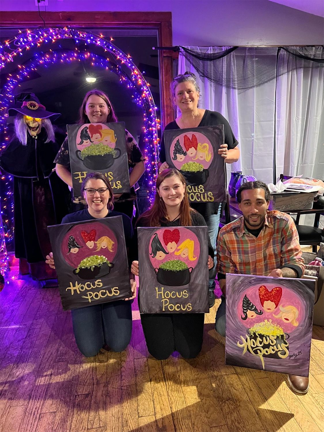 A group of people are posing for a picture with their Halloween paintings.