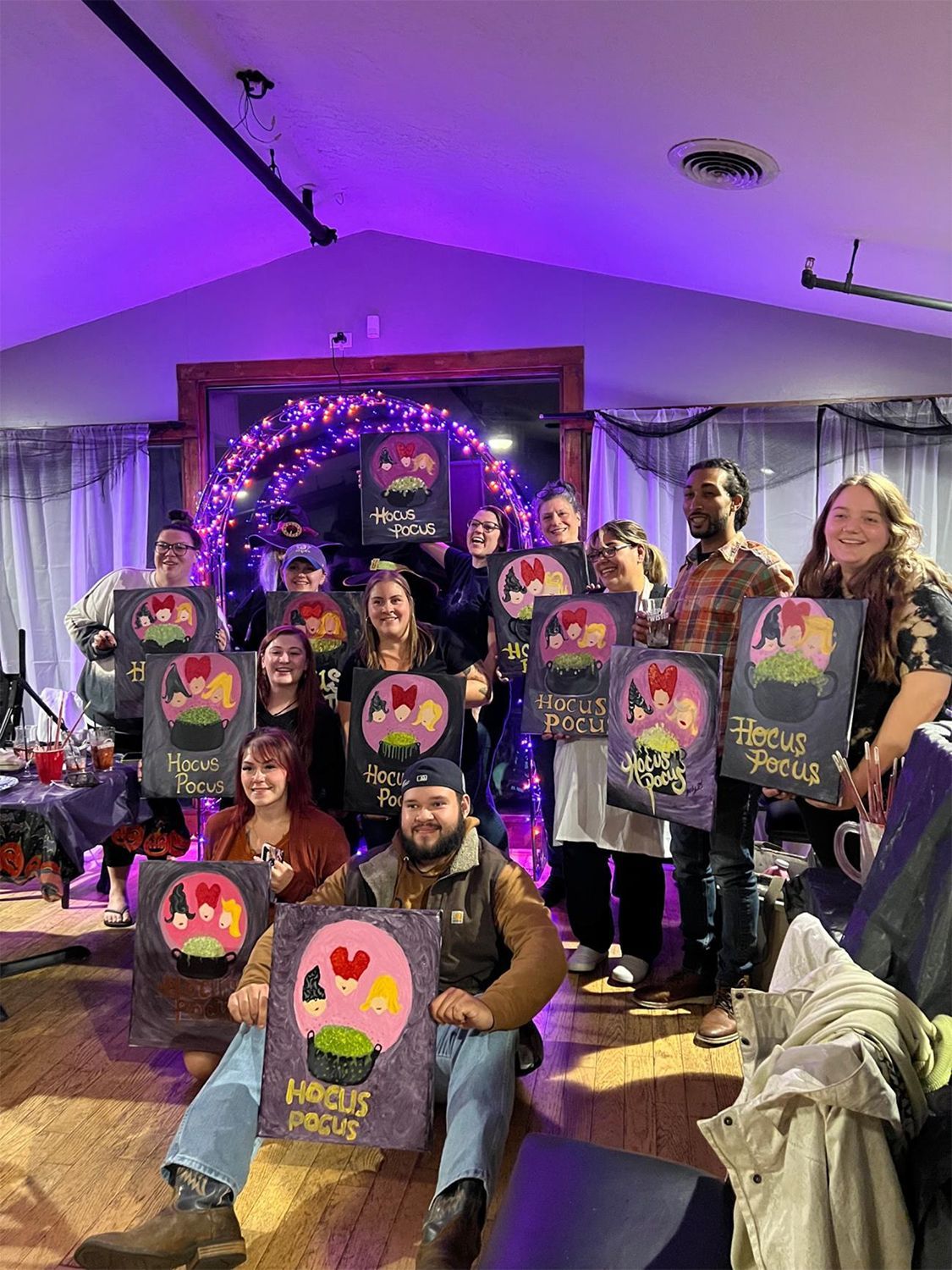 A group of people are posing for a picture with their Halloween paintings.
