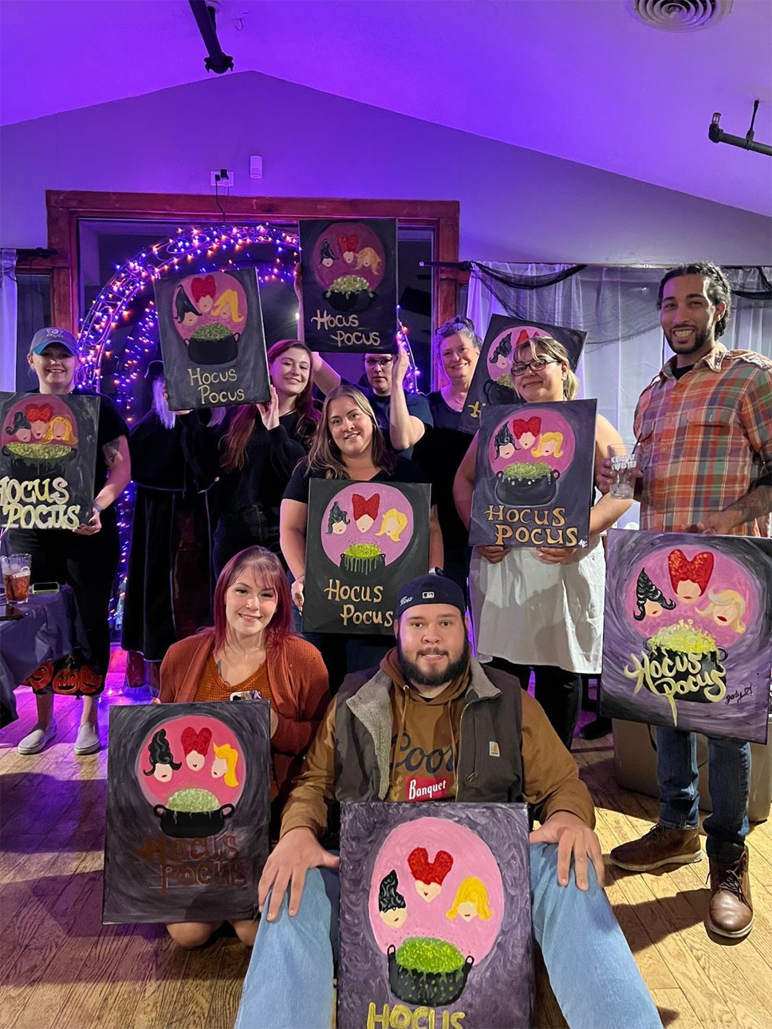 A group of people are posing for a picture with their Halloween paintings.