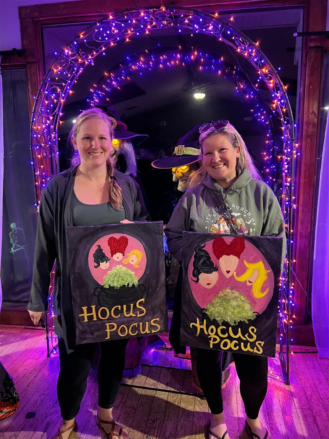 Two women are posing for a photo showing their Halloween artwork.