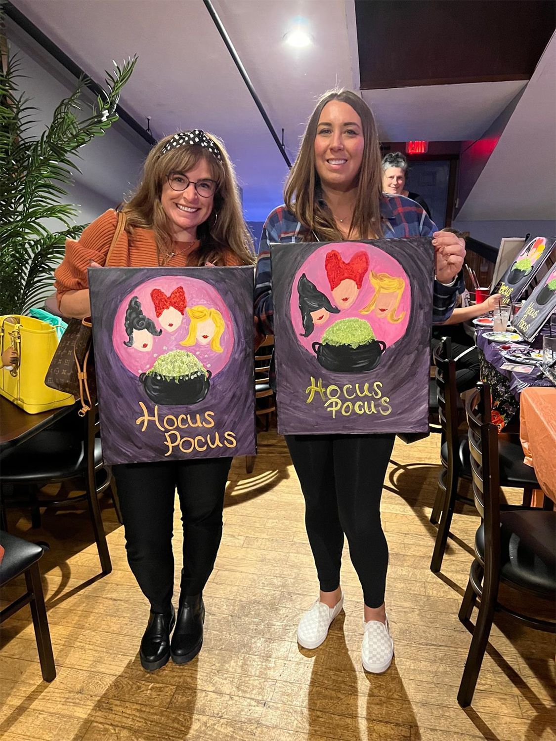 Two women are posing for a photo showing their Halloween artwork.