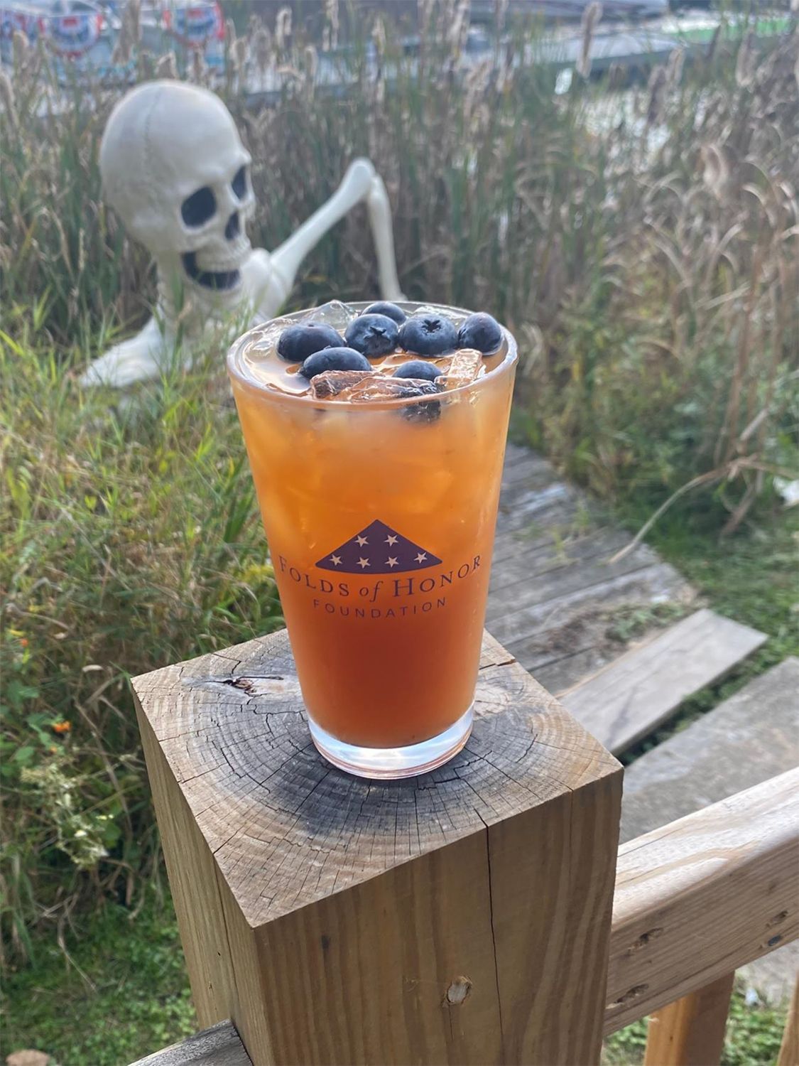 A drink with blueberries is sitting on a wooden block.