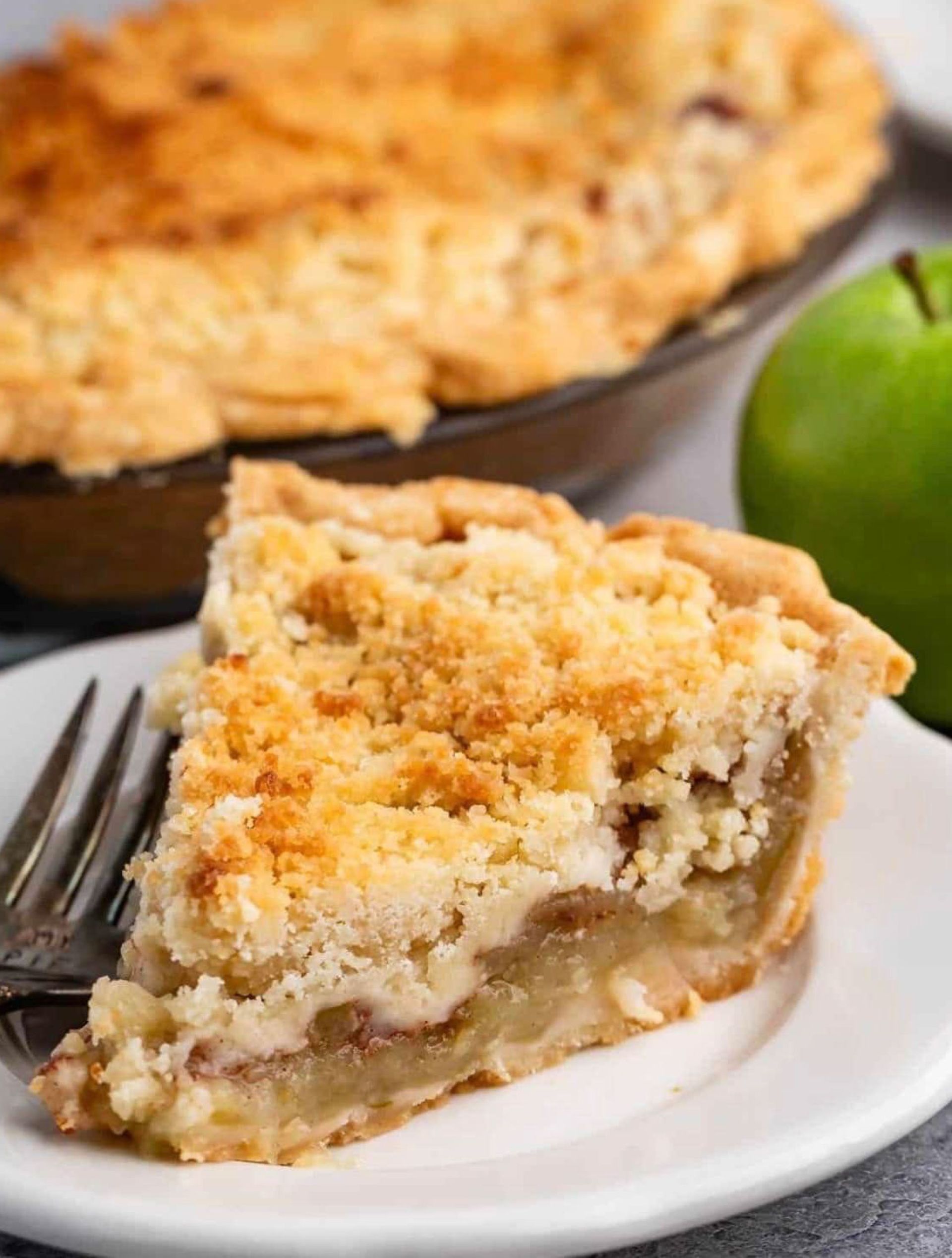 A slice of apple pie is on a white plate with a fork.