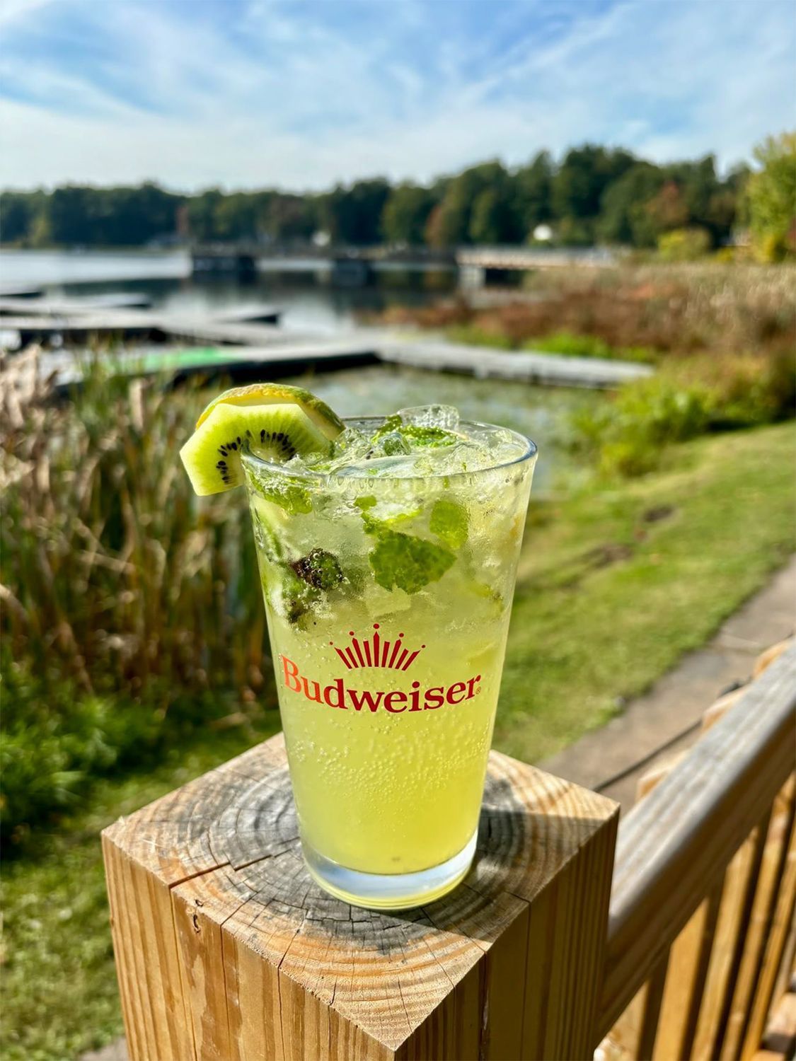 A drink in a Budweiser glass is sitting on a wooden post.