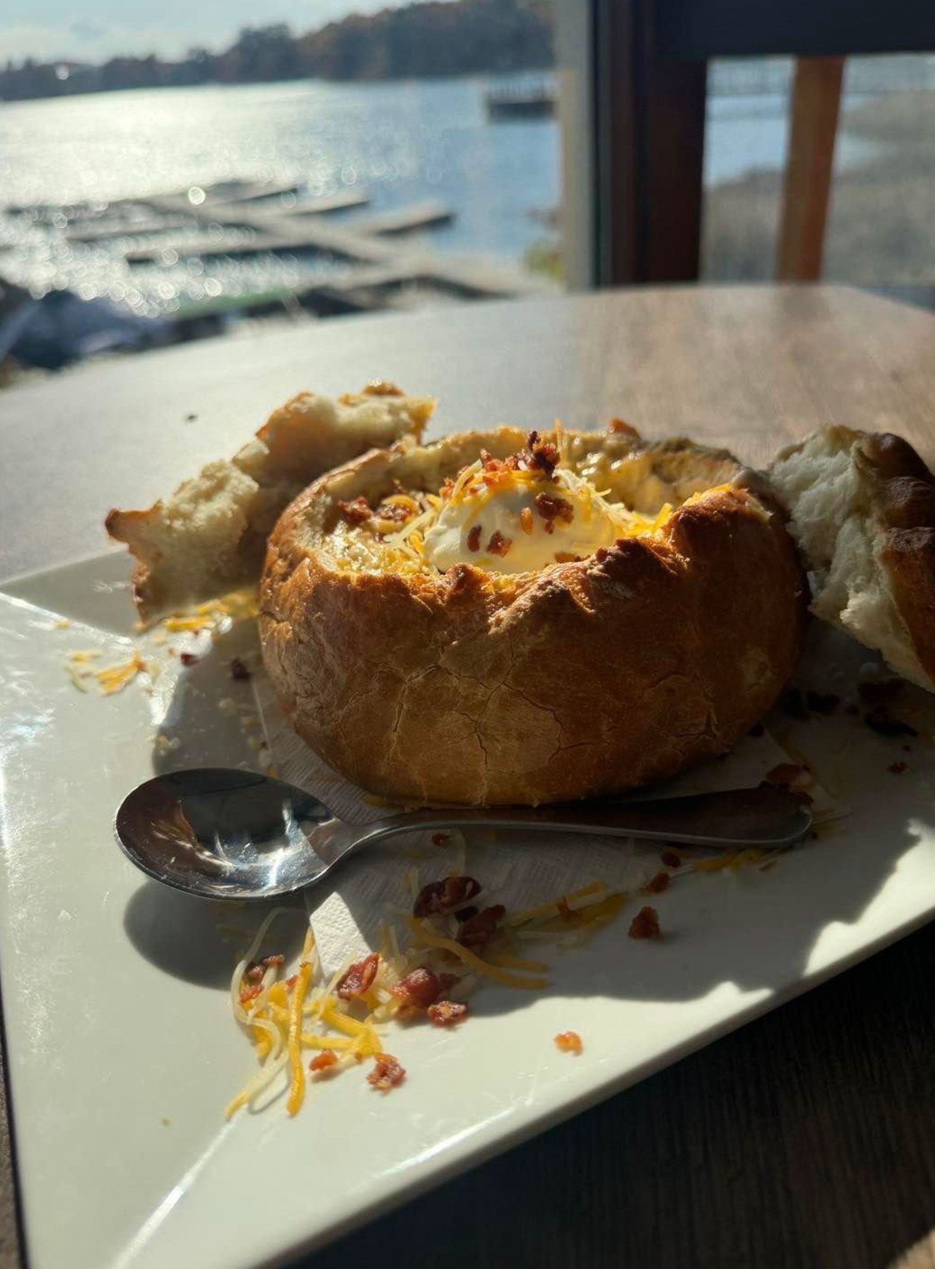 A white plate topped with a bread bowl of soup and a spoon.