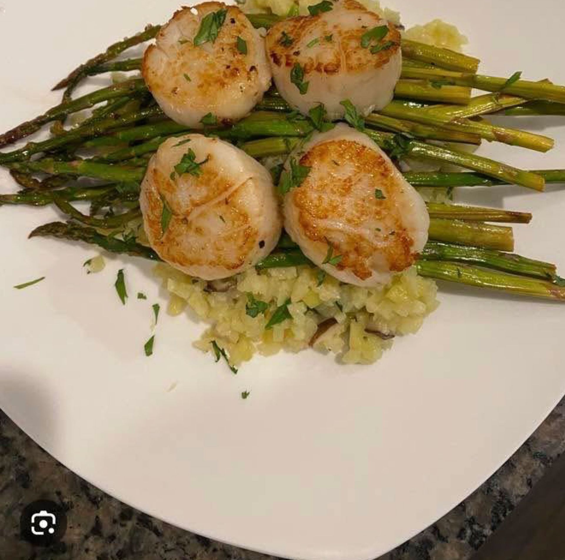 A white plate topped with scallops and asparagus on a table.