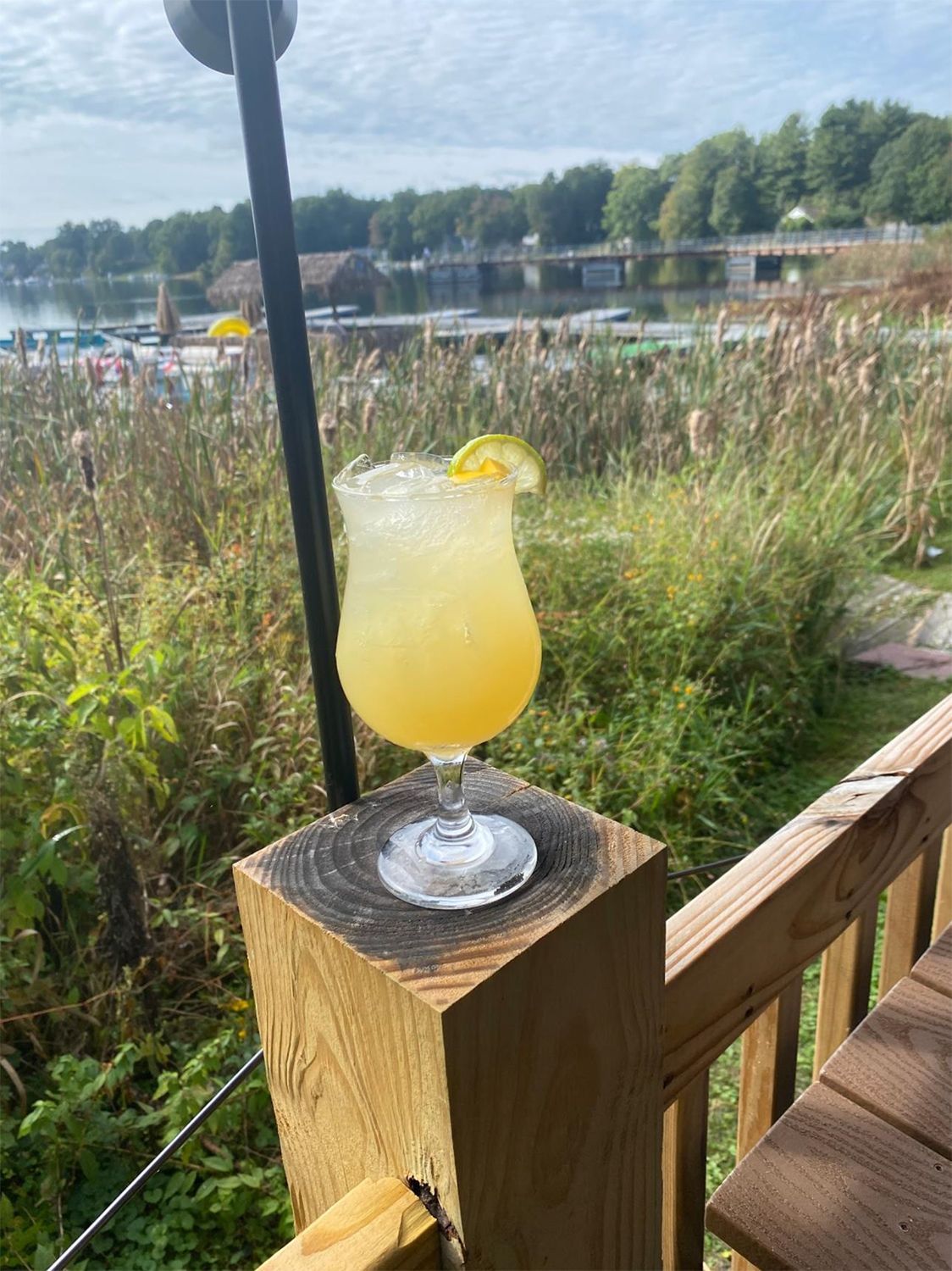 A drink is on a wooden post on a deck.