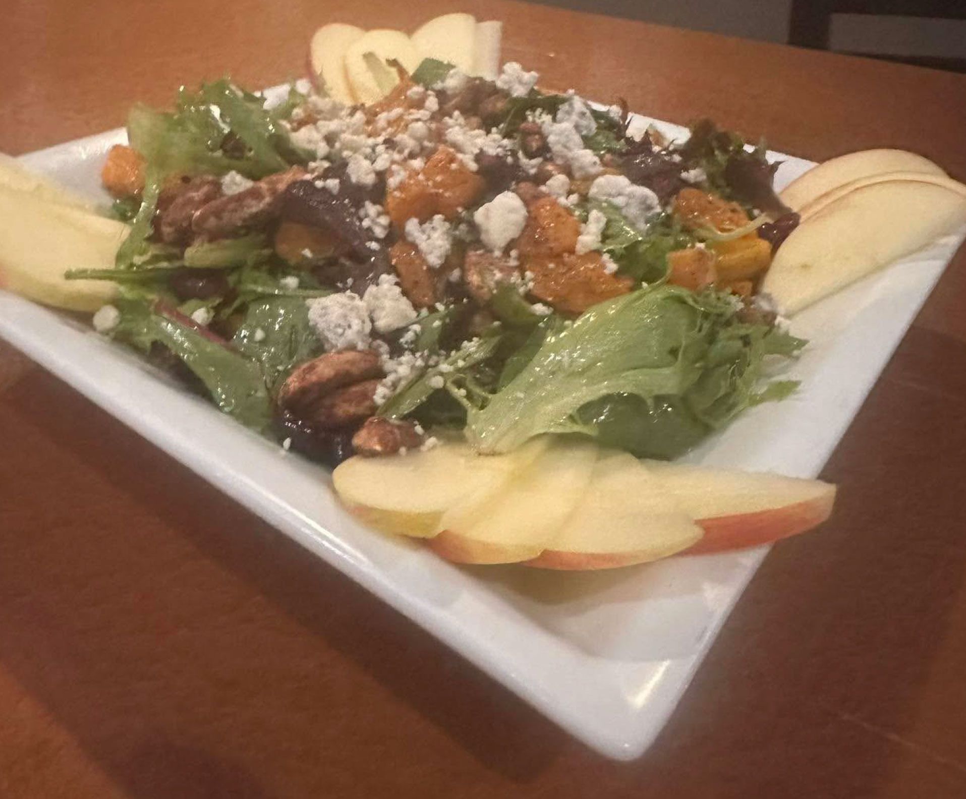 A salad with apples and nuts on a white plate on a table.
