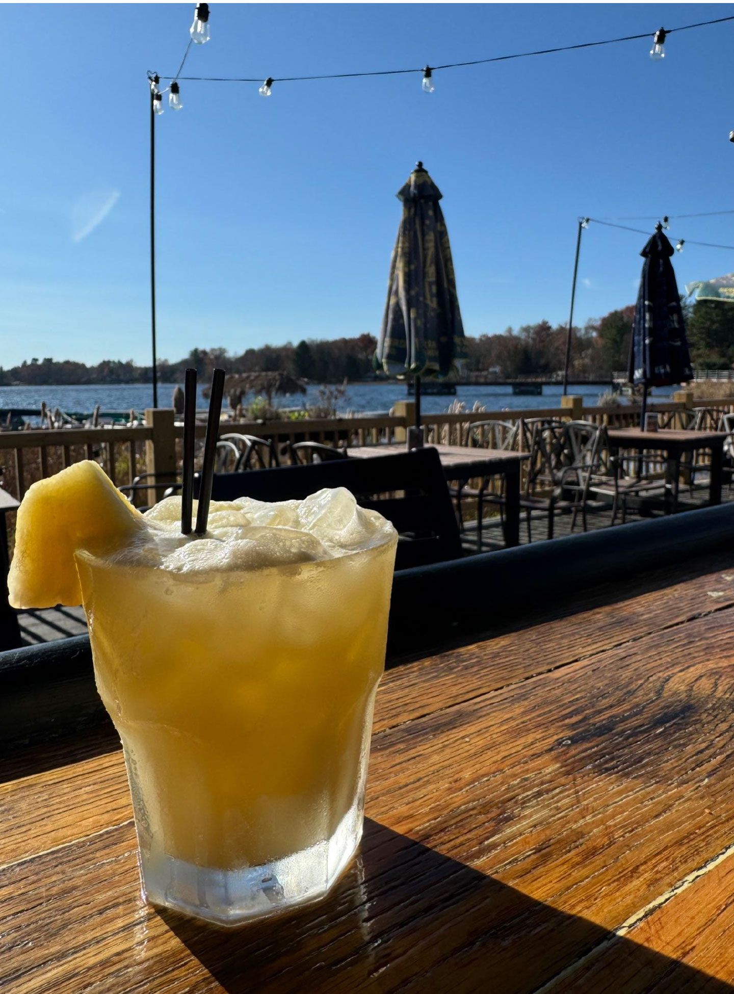 A drink is sitting on a wooden table in front of a lake.