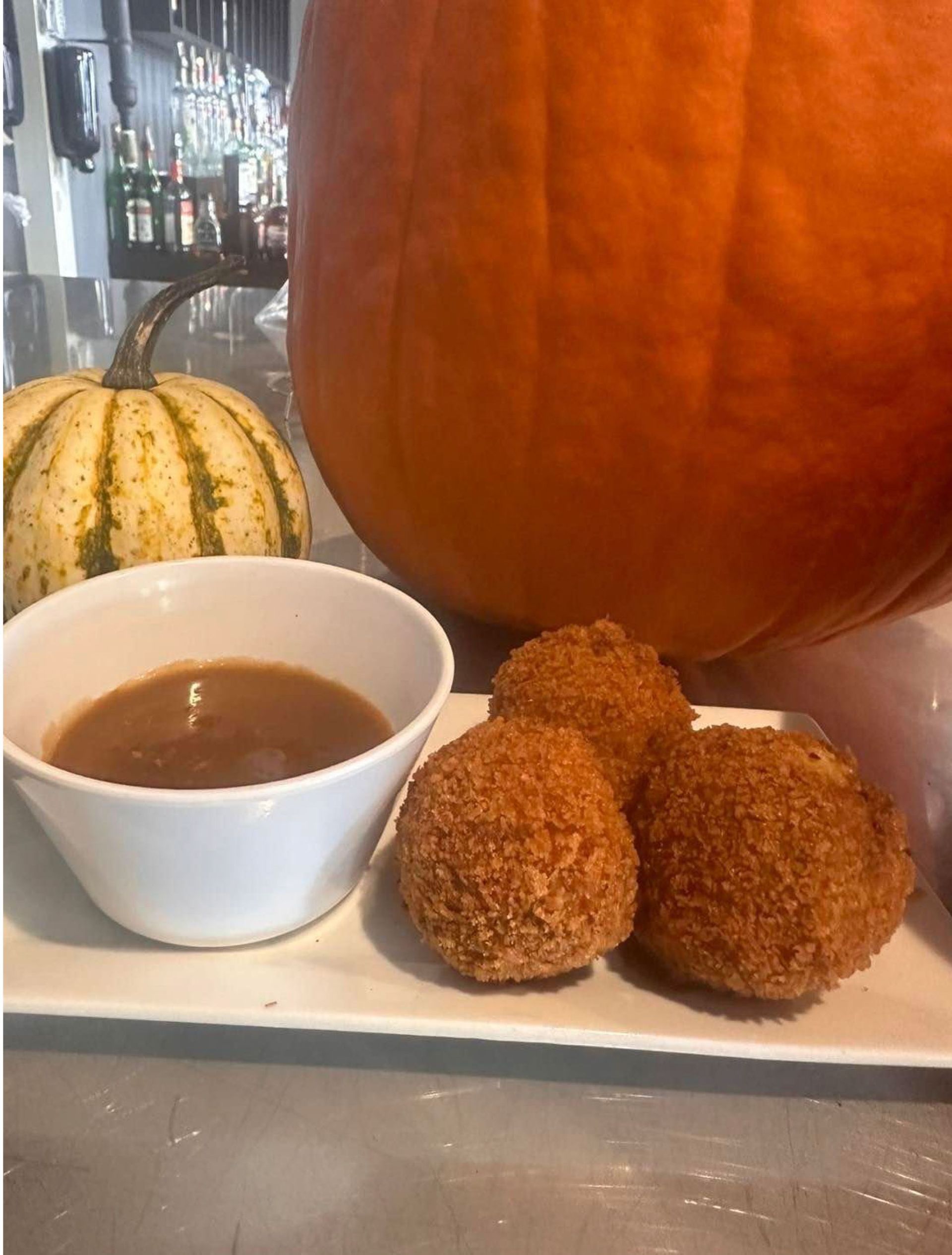 A plate of food with a bowl of sauce and a pumpkin in the background.