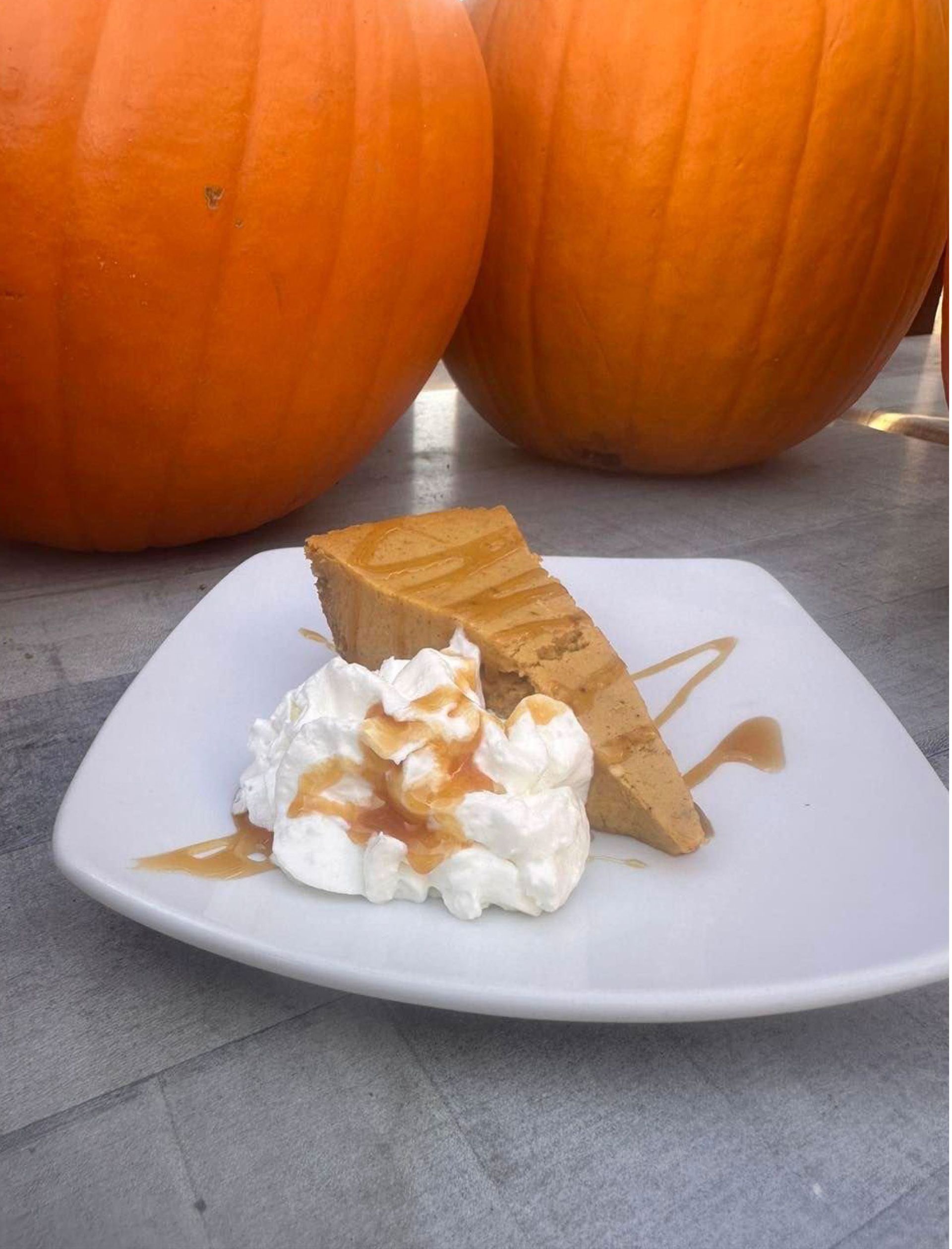 A slice of pumpkin pie with whipped cream and caramel sauce.