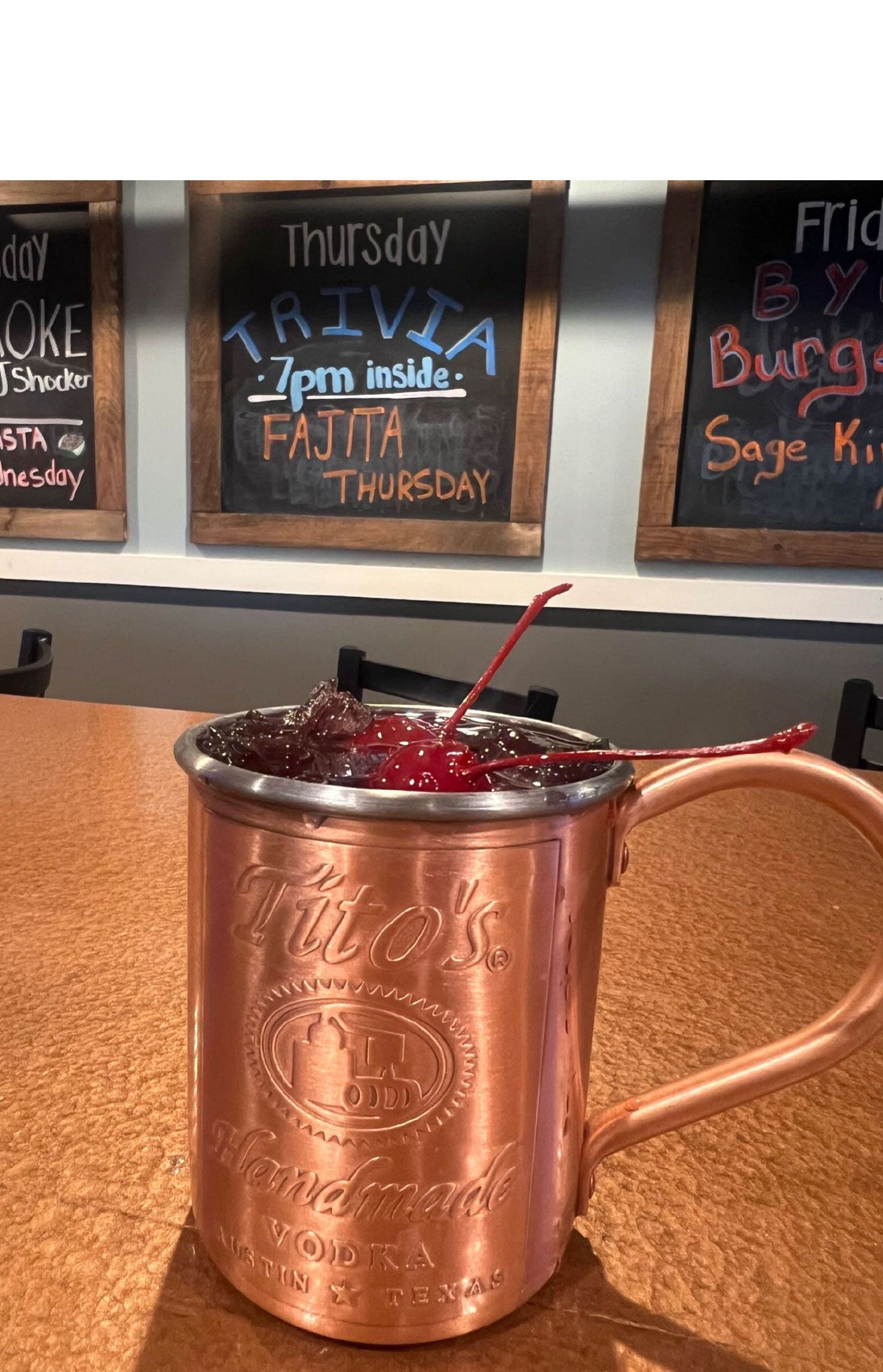 A copper mug filled with a drink and a cherry on a table.