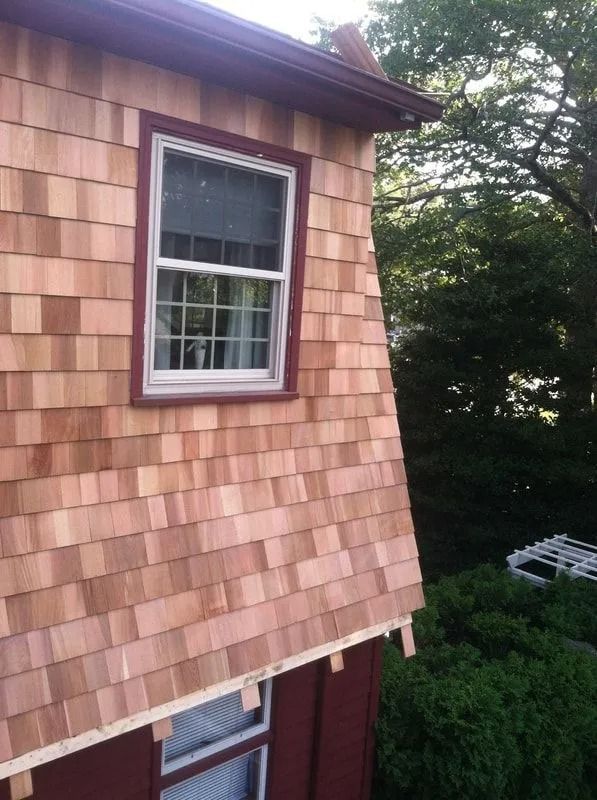 A two-story building exterior with new cedar shake siding and a window, viewed from an upper level.