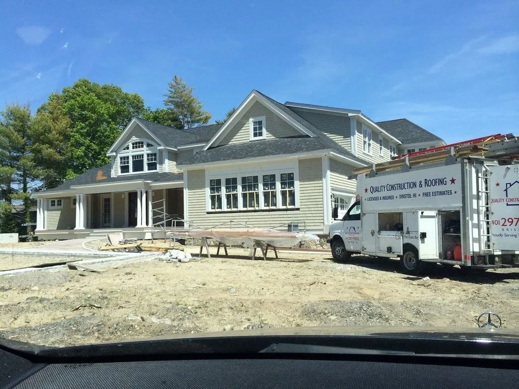 A partially completed light-colored house with a dark roof and a construction vehicle parked in the dirt front yard.