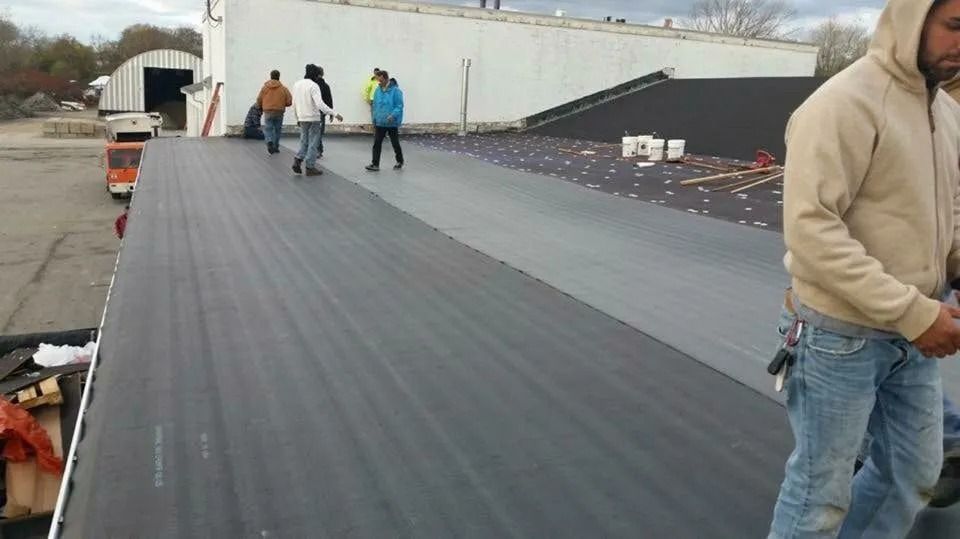 Construction workers on a flat commercial roof installing dark roofing membrane material.