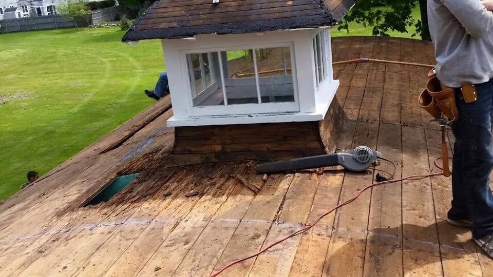 A person works on a wooden rooftop next to a cupola during a roof repair project.