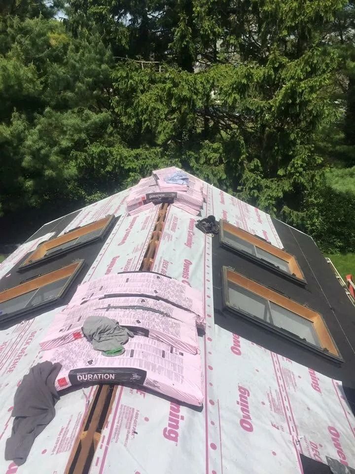 A roof undergoing construction with skylights installed and pink foam ridge vents laid out along the peak.