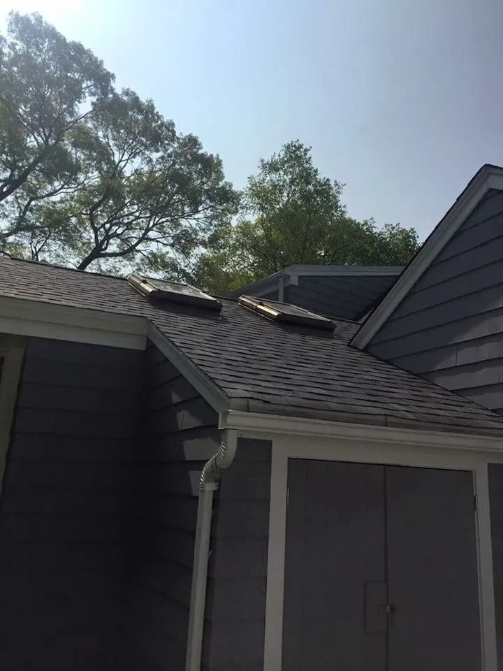 Two skylights installed on a gray shingled roof of a house with dark gray siding.