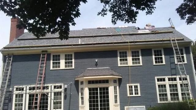 A blue two-story house under renovation with scaffolding on the roof and ladders leaning against the exterior walls.